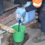 Worker wearing safety gloves pouring chemical from a container into a bucket kept on weighing scale