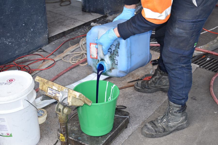 Worker wearing safety gloves pouring chemical from a container into a bucket kept on weighing scale