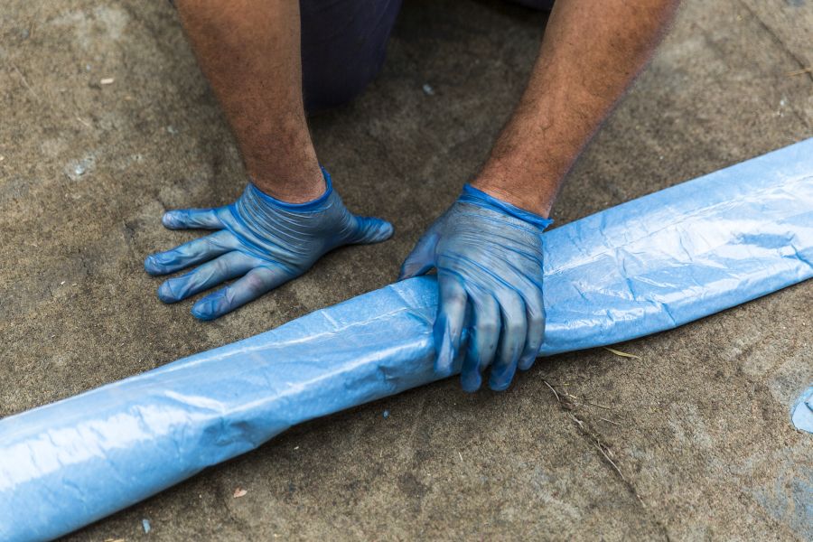 A man wearing blue coloured safety gloves and holding a Pipe