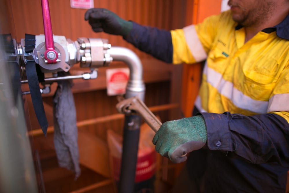 Picture of miner male hand plumber wearing a industrial glove performing fastening hydraulic hose with pipe wrench into a corner connector construction mine site, Perth, Australia